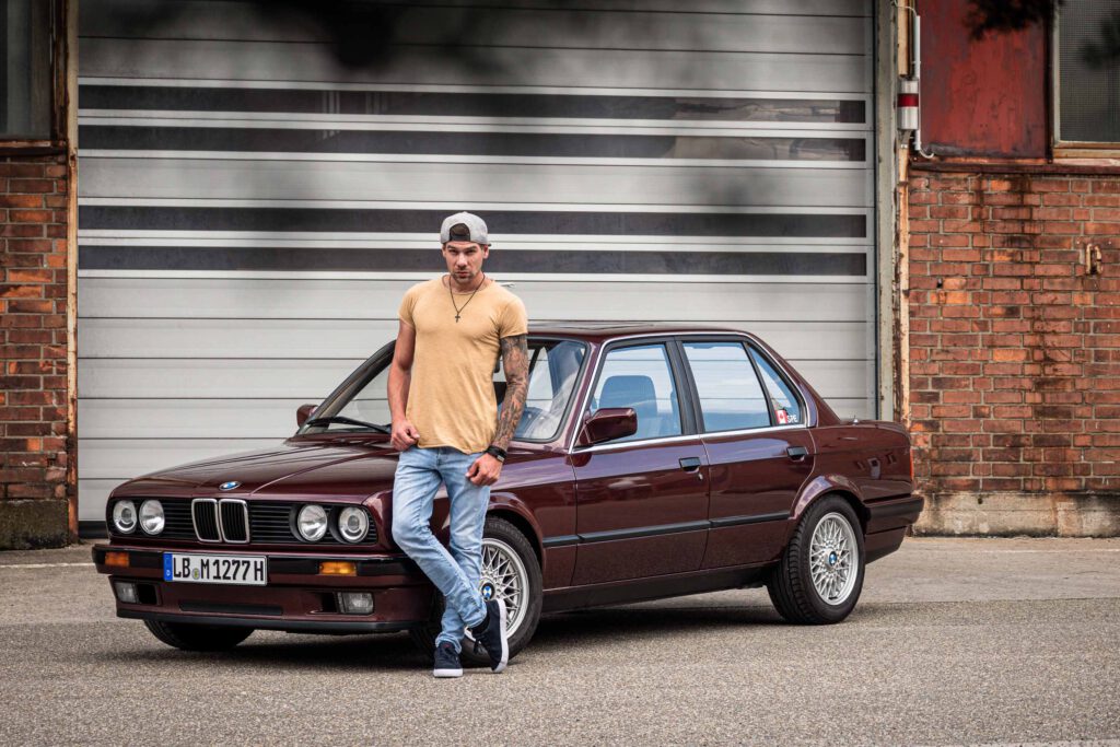 Mann mit rotem BMW E30 vor Rolltor.